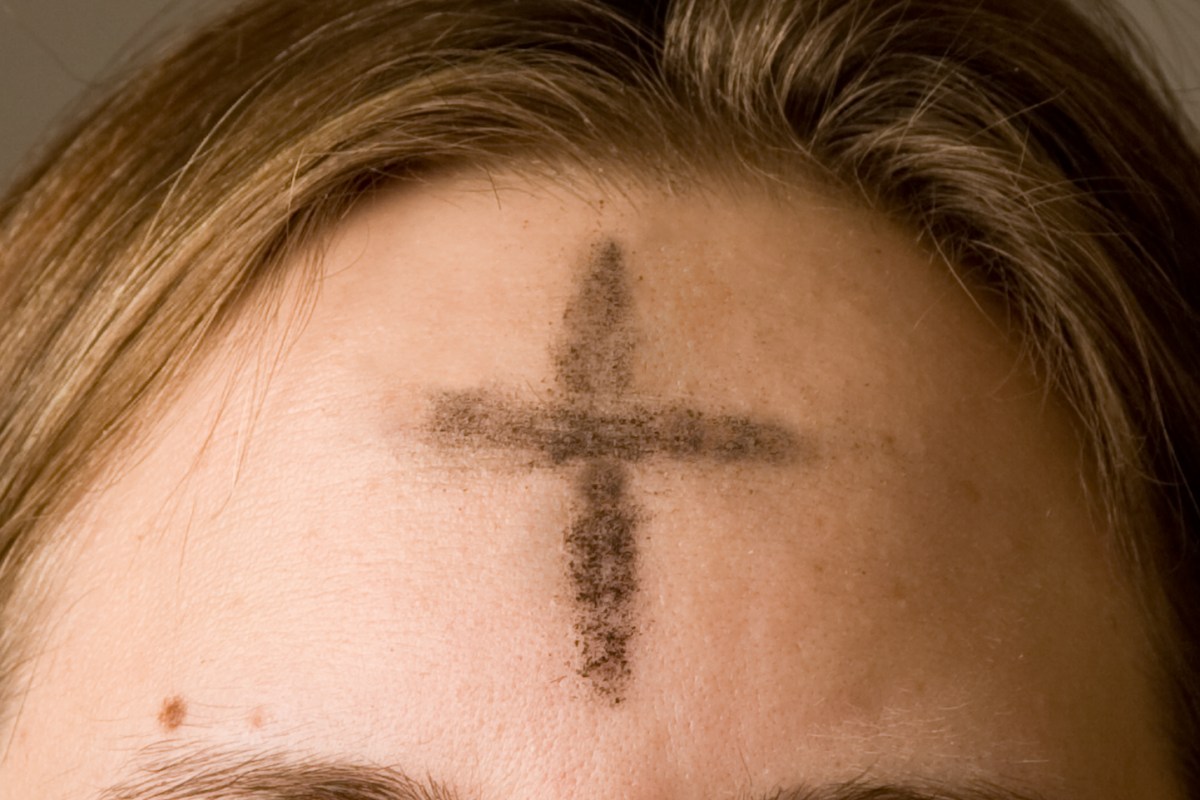 a white person has dark ashes in the shape of a cross on their forehead